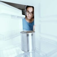A Generic Can of Food in an Otherwise Empty Freezer With a Girl Looking in Dubiously