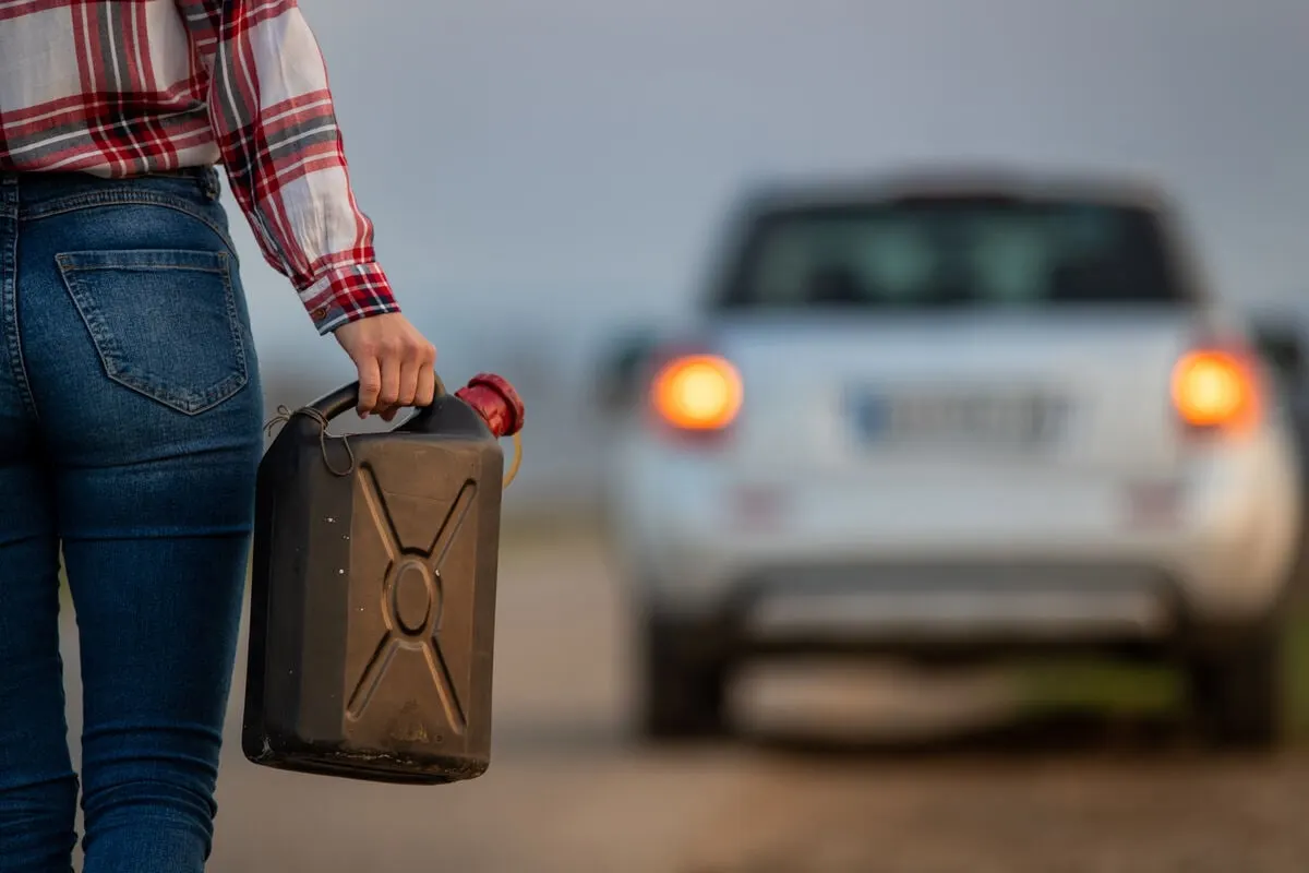 Close up of a woman holding a gas can and walking toward her car