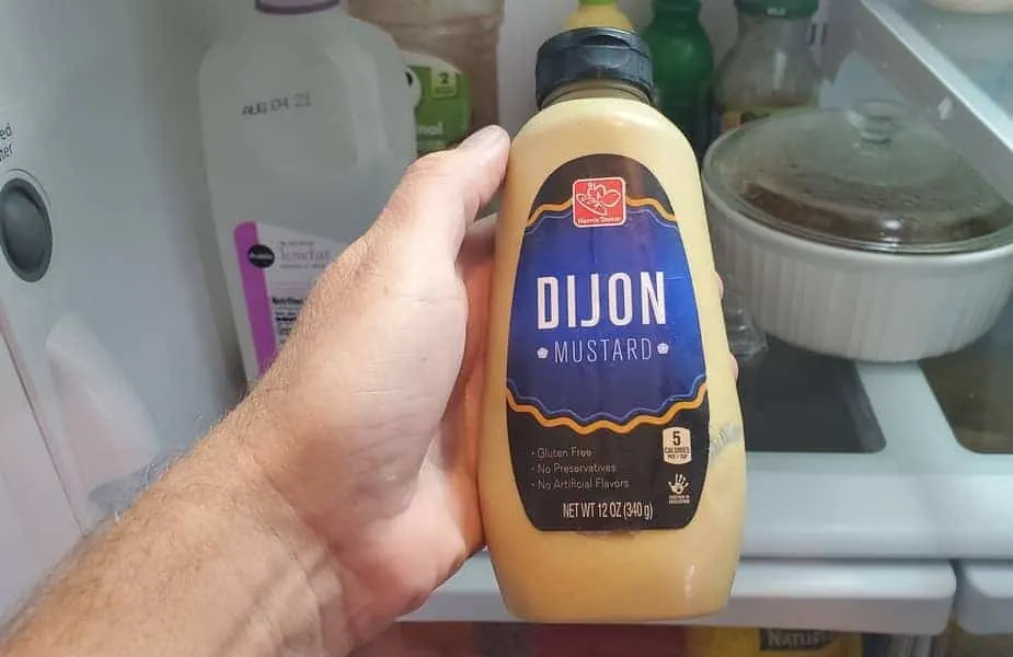 Dijon Mustard Held in Front of a Fridge