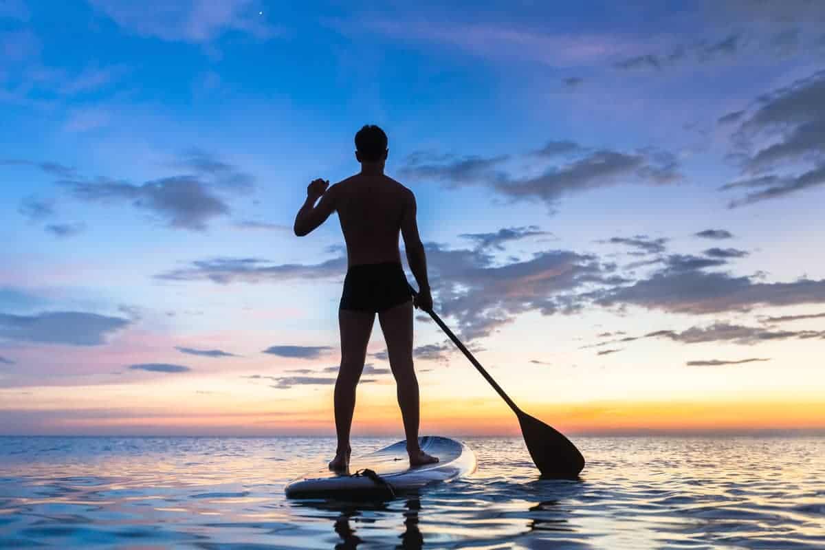 Silhouette of stand up paddle boarder at sunset on a flat warm quiet sea