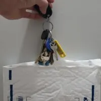 Hand Holding Multiple Keys Above a USPS Bubble Mailer
