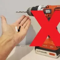 Hand-Holding-a-Plastic-Anchor-and-a-Screw-Next-to-a-Drill-With-a-Red-X-Over-It