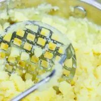 Lumpy Mashed Potatoes in a Pot With a Potato Masher