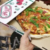 Pizza inside a cardboard box in front of a wooden heated pizza oven