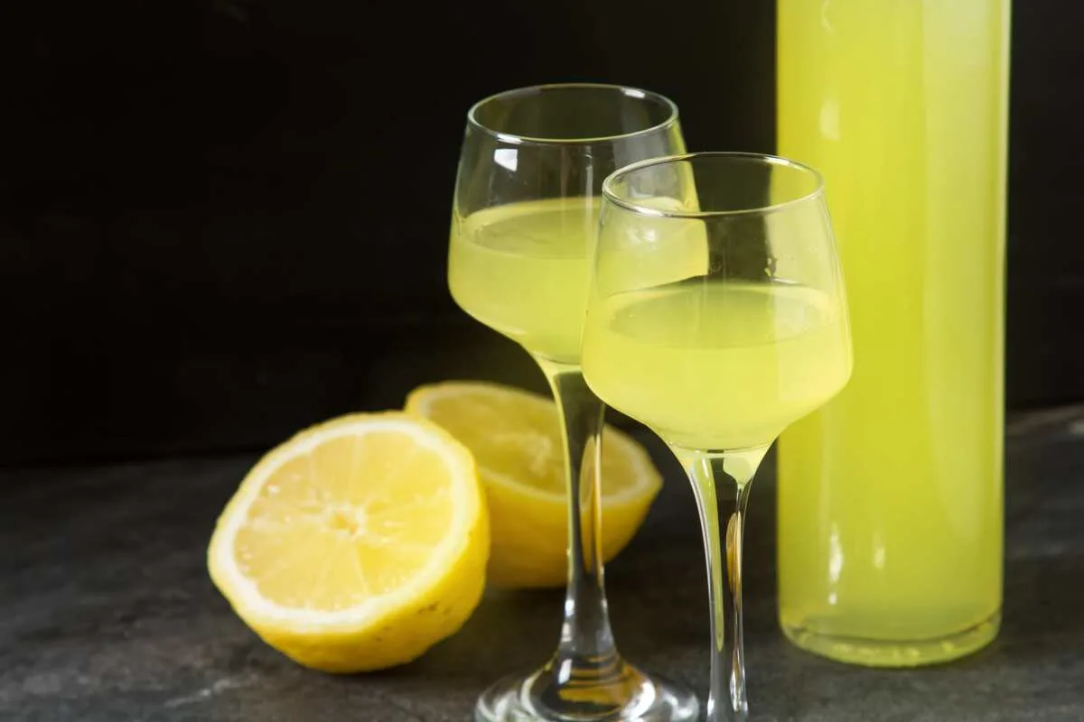 Bottle of limoncello next to two glasses and a lemon cut in half