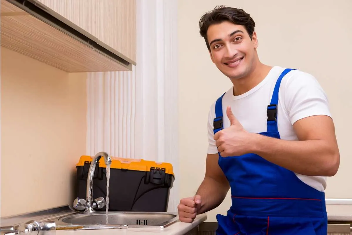 Young plumber giving a thumbs up in front of a kitchen sink with the water running