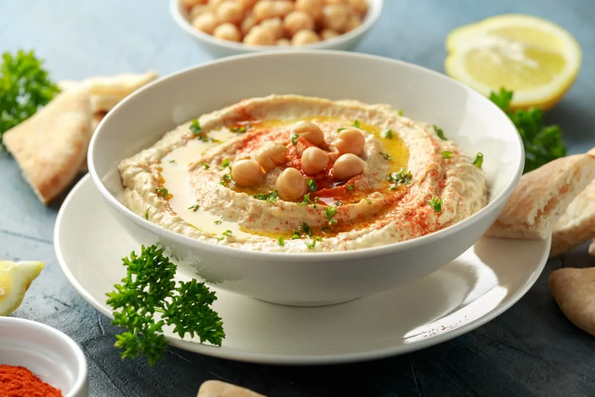 A bowl of hummus with bread and tomatoes on the side