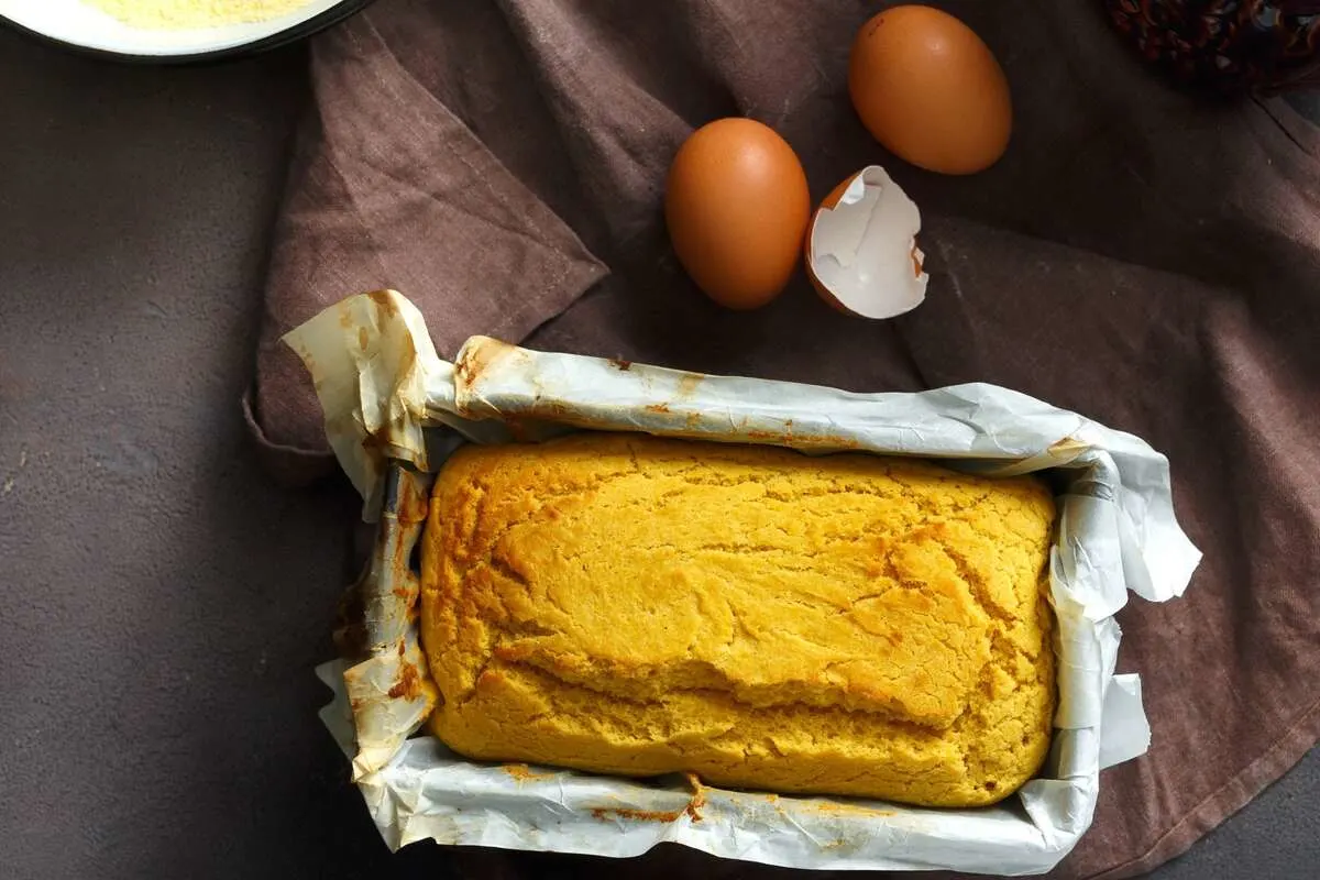Fresh loaf of homemade corn bread with eggs nearby