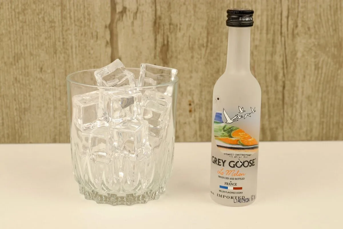 A small bottle of grey goose vodka with a glass of ice nearby