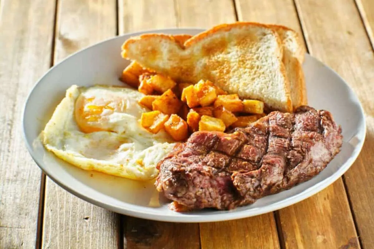 Steak and eggs breakfast with toast and homestyle potatoes on wooden table
