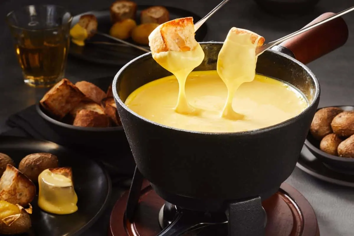 Two pieces of bread being dipped into a cheese fondue